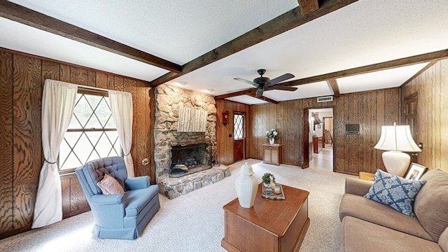 living room featuring healthy amount of natural light, a stone fireplace, wood walls, beam ceiling, and a ceiling fan