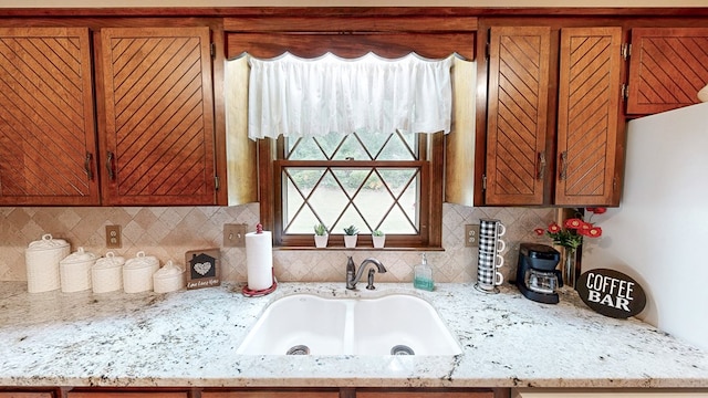 kitchen featuring a sink, brown cabinets, tasteful backsplash, and light stone counters