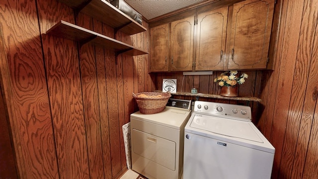 laundry area with washing machine and clothes dryer, cabinet space, wooden walls, and a textured ceiling