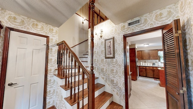 staircase featuring wallpapered walls, a textured ceiling, tile patterned flooring, and baseboards
