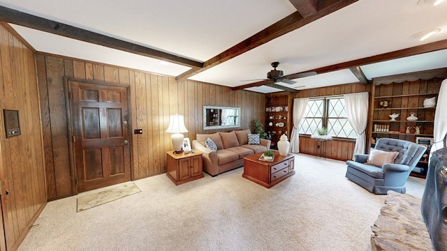 living room featuring beam ceiling, wood walls, a ceiling fan, and light carpet