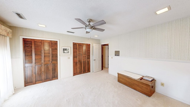 unfurnished bedroom featuring multiple closets, carpet, a ceiling fan, and wallpapered walls