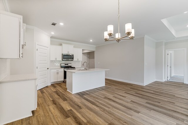 kitchen featuring appliances with stainless steel finishes, ornamental molding, wood-type flooring, a chandelier, and white cabinetry