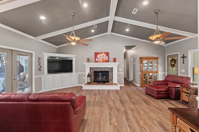 living room with vaulted ceiling with beams, a stone fireplace, light hardwood / wood-style floors, and ceiling fan