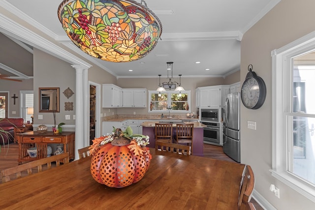 dining area featuring decorative columns, ornamental molding, sink, and an inviting chandelier