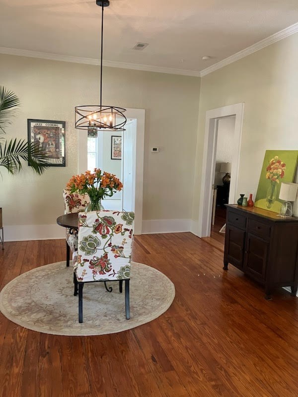 dining space with visible vents, baseboards, wood finished floors, crown molding, and a notable chandelier