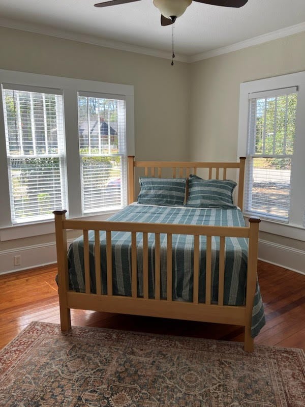 bedroom with wood-type flooring, multiple windows, and crown molding