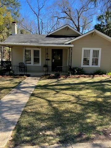 view of front of home featuring covered porch, a chimney, and a front yard