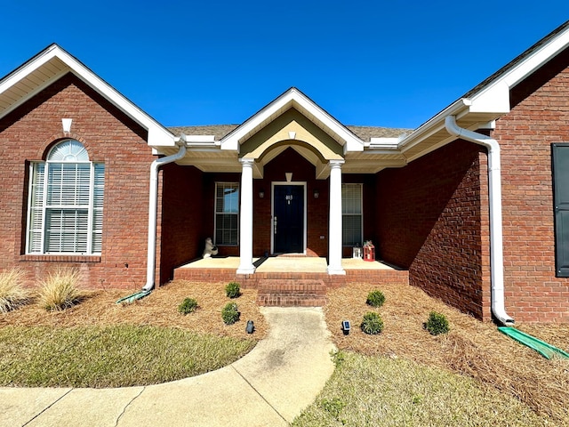 doorway to property with a porch and brick siding