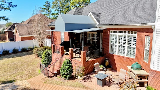 back of house featuring brick siding, roof with shingles, a patio area, fence, and a fire pit