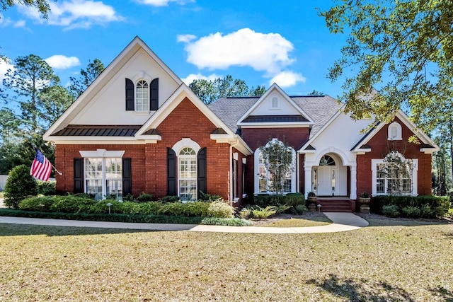 view of front of house with a front yard, a standing seam roof, and brick siding