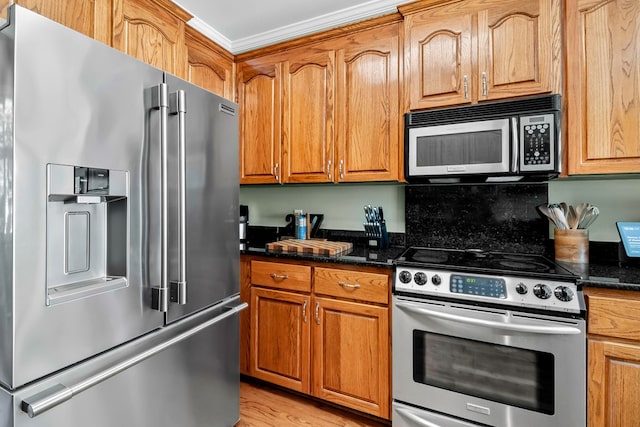 kitchen with appliances with stainless steel finishes, brown cabinetry, light wood-style flooring, and dark stone countertops