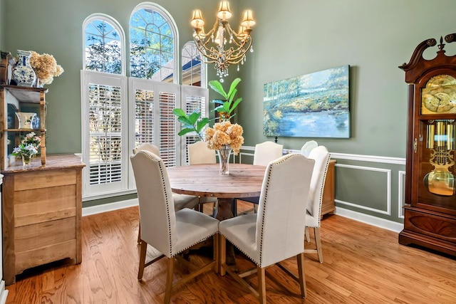 dining area with light wood-style floors, a chandelier, a decorative wall, and wainscoting