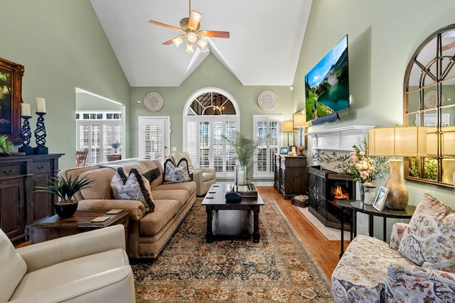 living room with light wood-style floors, ceiling fan, a premium fireplace, and high vaulted ceiling