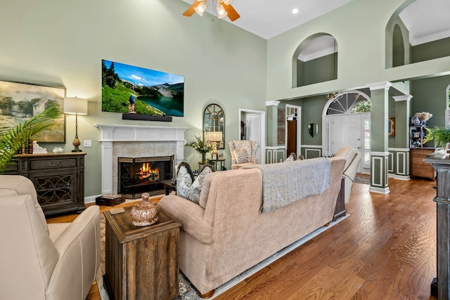 living area featuring a high ceiling, a fireplace, wood finished floors, a ceiling fan, and decorative columns