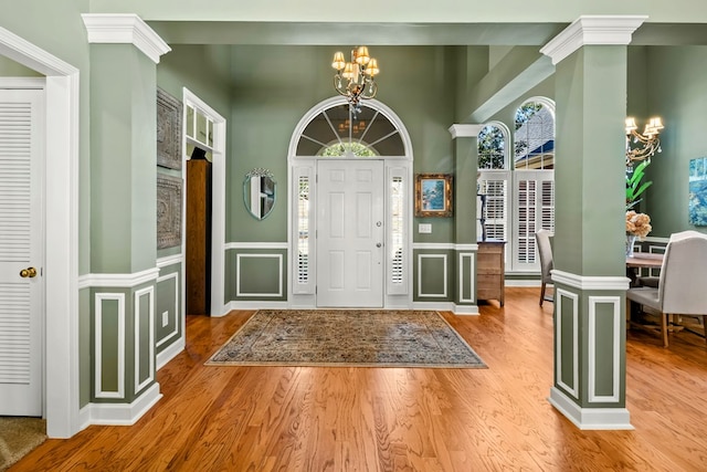 foyer featuring a chandelier, wood finished floors, decorative columns, and a decorative wall