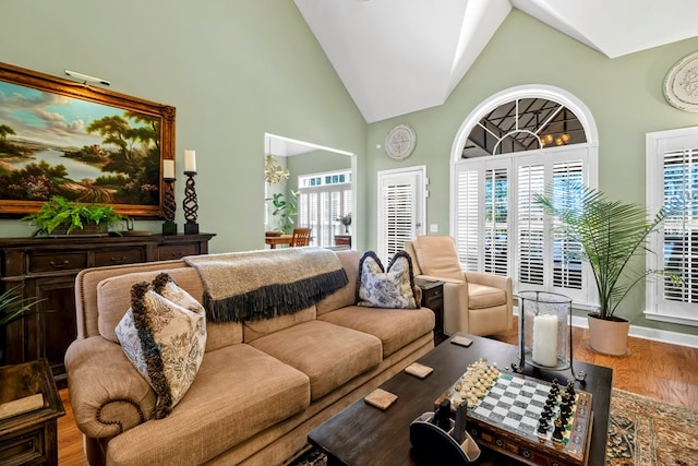 living area with high vaulted ceiling, wood finished floors, and baseboards