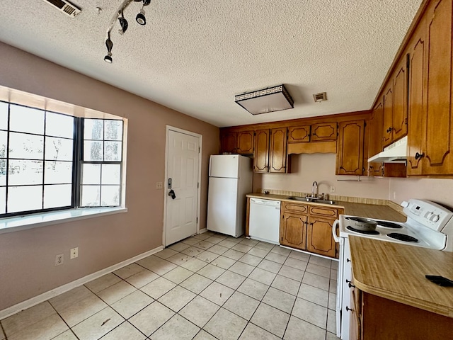 kitchen featuring white appliances, light tile patterned floors, under cabinet range hood, a sink, and brown cabinetry