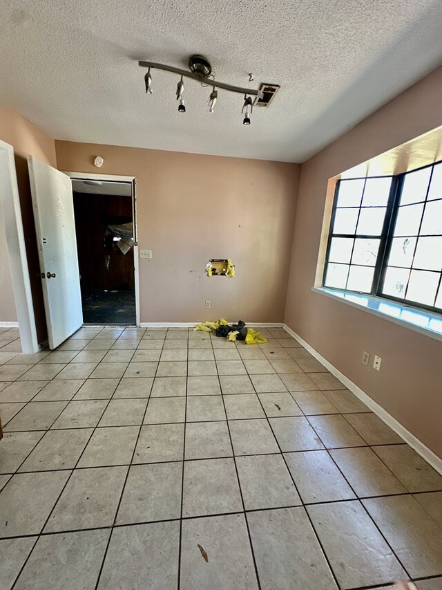 empty room with baseboards, a textured ceiling, rail lighting, and light tile patterned floors