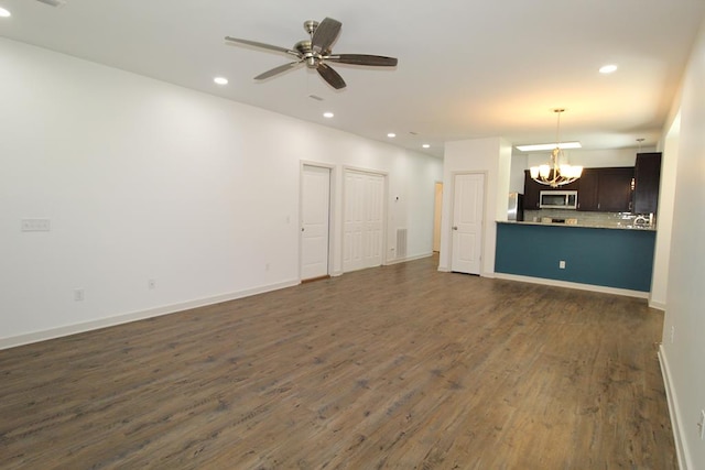 unfurnished living room featuring ceiling fan with notable chandelier and dark wood-type flooring