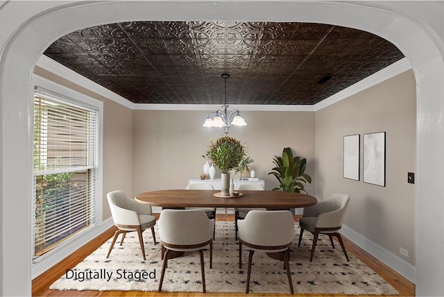 dining space with wood-type flooring, an inviting chandelier, and crown molding