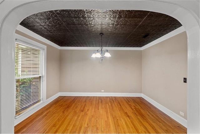 empty room with hardwood / wood-style flooring, an inviting chandelier, and crown molding