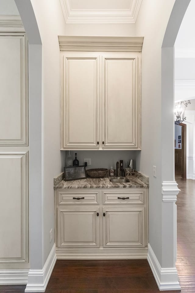 bar featuring baseboards, dark wood finished floors, arched walkways, a sink, and indoor bar