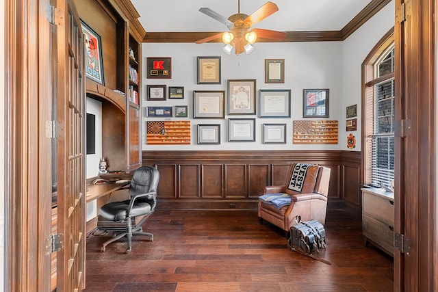 home office with dark wood-style floors, a ceiling fan, a wainscoted wall, ornamental molding, and built in desk