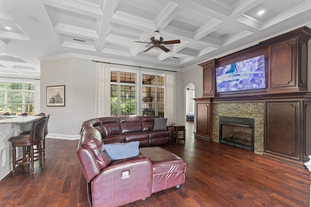 living area with coffered ceiling, beam ceiling, dark wood-style flooring, ceiling fan, and a stone fireplace