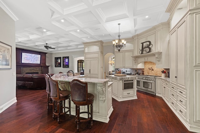 kitchen featuring cream cabinets, an island with sink, double oven range, and arched walkways