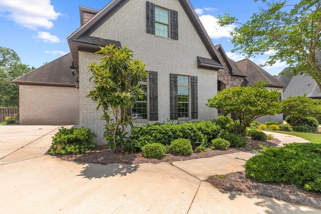 view of property exterior featuring a garage, brick siding, driveway, and a shingled roof