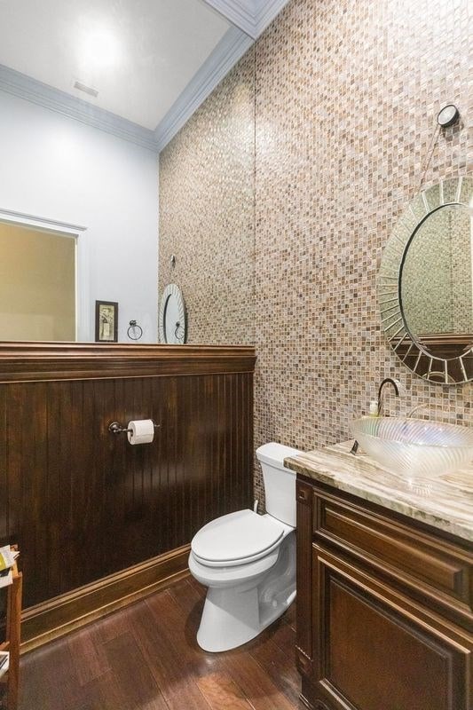 bathroom featuring toilet, wood finished floors, tile walls, crown molding, and vanity