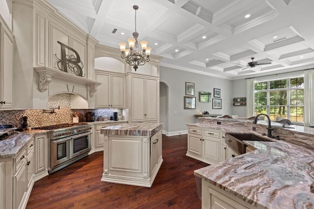 kitchen with double oven range, arched walkways, a sink, a large island, and cream cabinetry