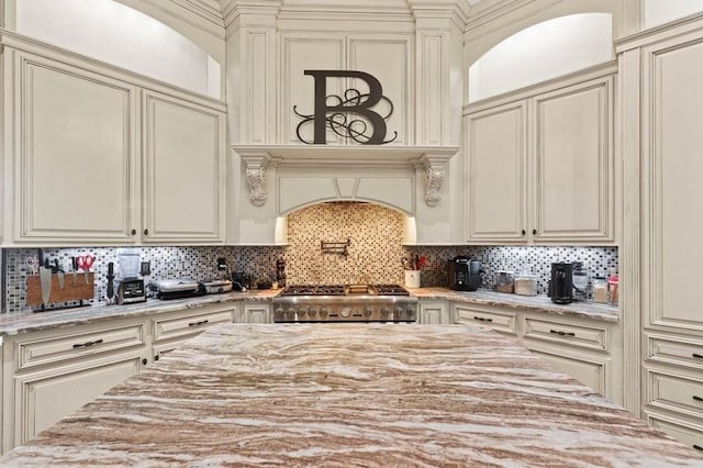 kitchen with tasteful backsplash, cream cabinetry, light stone countertops, and range