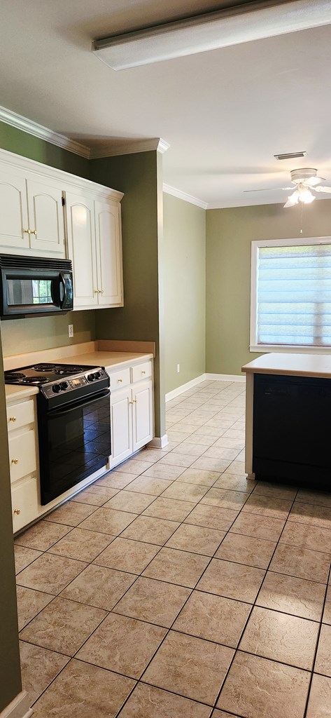 301 Roslyn Glen Way, Dothan, AL 36305 - kitchen featuring black microwave, gas range oven, ornamental molding, light tile patterned floors, and white cabinetry