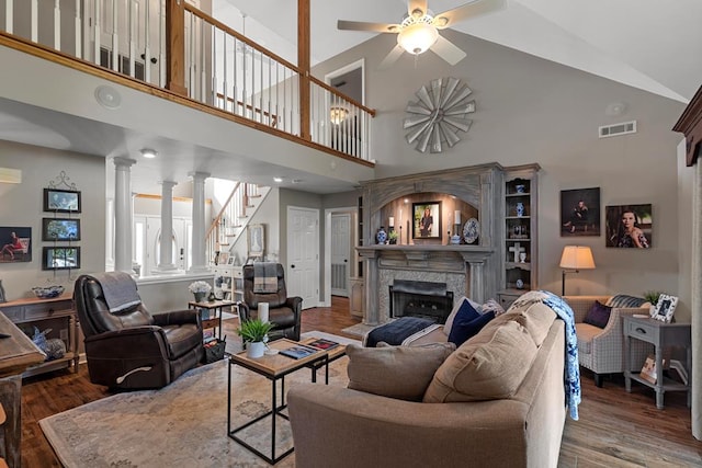 living room with ornate columns, wood-type flooring, high vaulted ceiling, and a premium fireplace