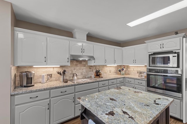 kitchen featuring white cabinetry, a center island, light stone countertops, stainless steel appliances, and backsplash