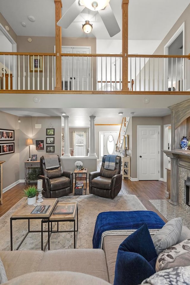 living room with ceiling fan, light hardwood / wood-style floors, a premium fireplace, and decorative columns