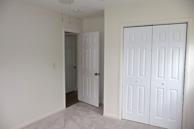 unfurnished bedroom featuring light carpet, a closet, and baseboards