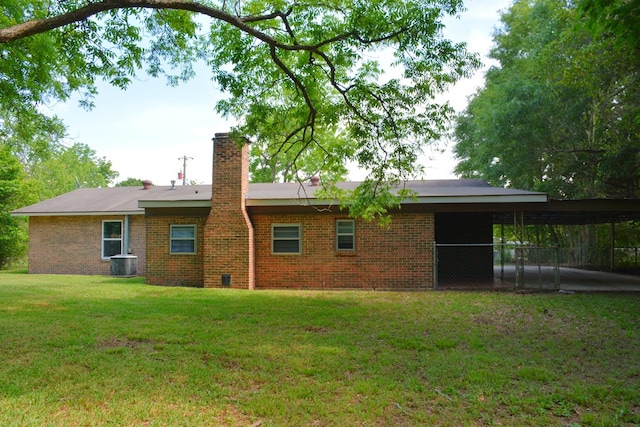 back of property featuring central AC, an attached carport, a chimney, brick siding, and a yard