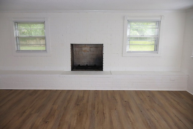 detailed view of crown molding, wood finished floors, a brick fireplace, and brick wall