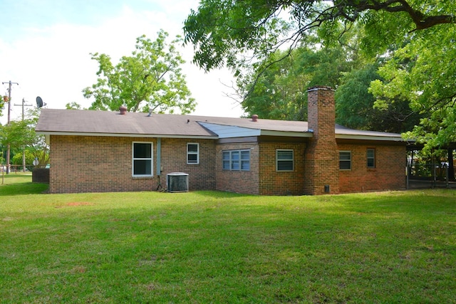 rear view of house with cooling unit, a chimney, brick siding, and a yard
