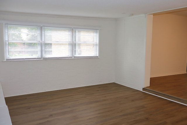 empty room featuring brick wall, plenty of natural light, crown molding, dark wood-style flooring, and a smoke detector