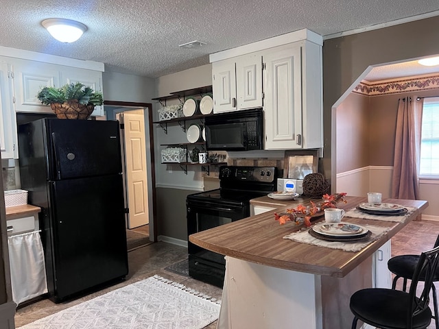 kitchen with black appliances, a breakfast bar, white cabinets, and a textured ceiling