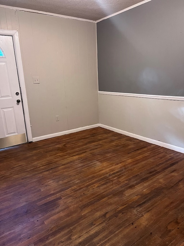 spare room featuring a textured ceiling, wooden walls, dark hardwood / wood-style floors, and ornamental molding