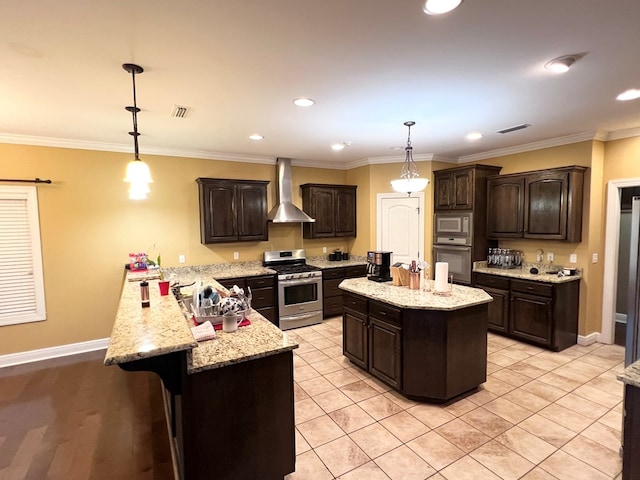 kitchen with dark brown cabinetry, a center island, wall chimney exhaust hood, stainless steel appliances, and pendant lighting