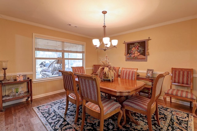 dining area featuring a chandelier, ornamental molding, wood finished floors, and wainscoting