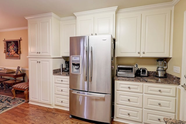 kitchen featuring stainless steel fridge with ice dispenser, light wood-style flooring, dark stone counters, white cabinets, and ornamental molding