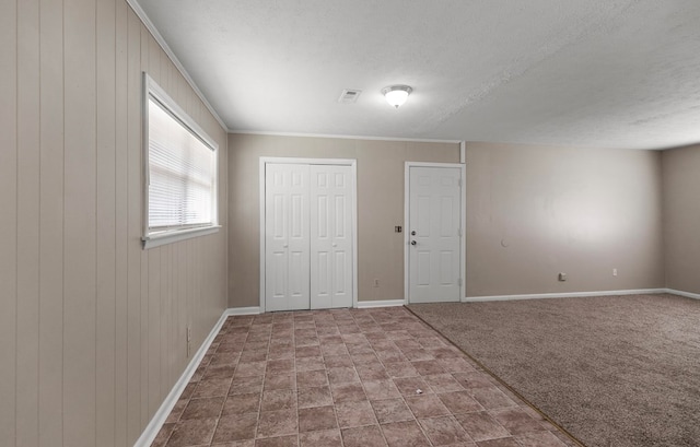 carpeted empty room featuring crown molding, wooden walls, and a textured ceiling