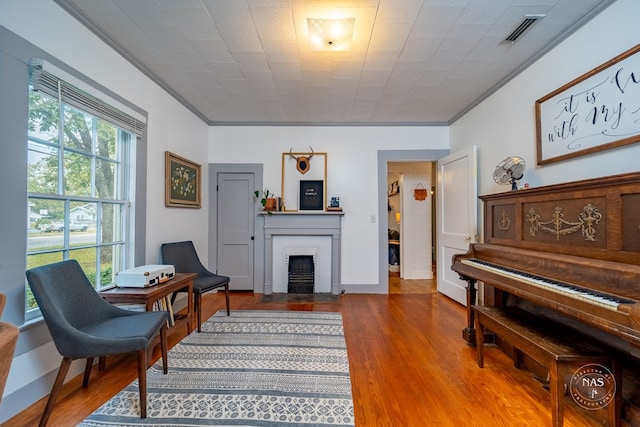 living area featuring wood-type flooring, crown molding, and a brick fireplace